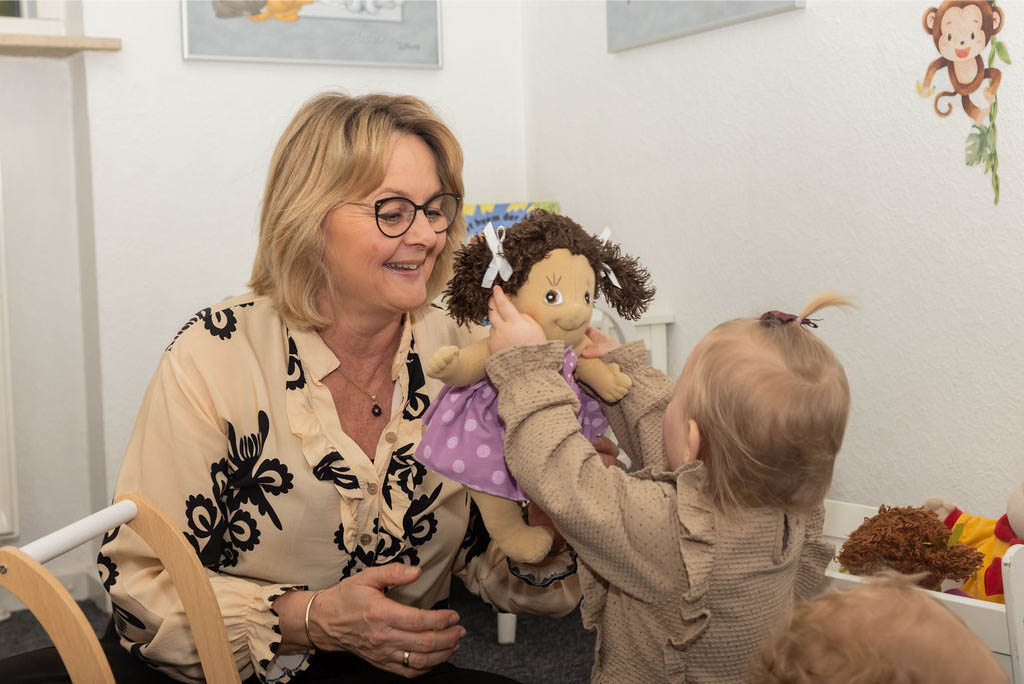 Begejret barn giver sin dukke til Krista Sønderup i hendes private børnepasning